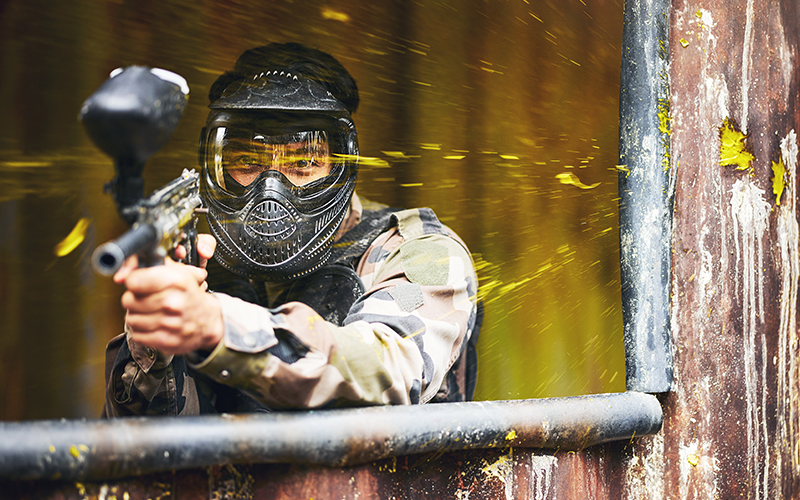A paintballer narrowly missing a paintball impact on a wall.